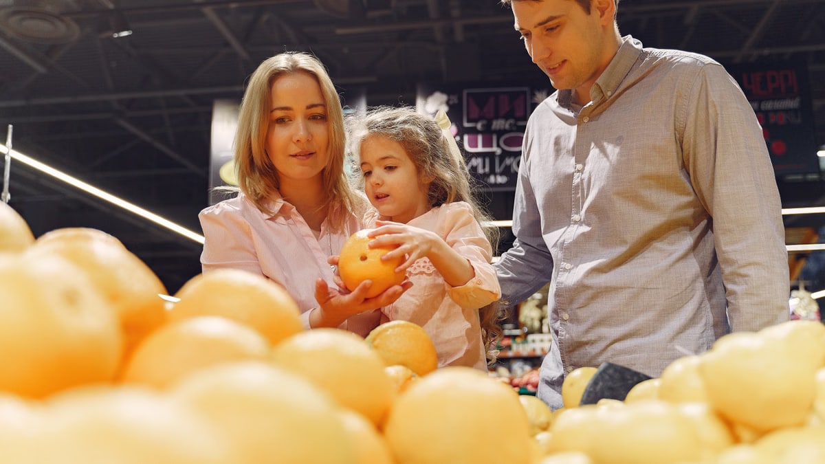 Parents and child selecting fresh oranges together at the supermarket. Captures family bonding and healthy shopping.